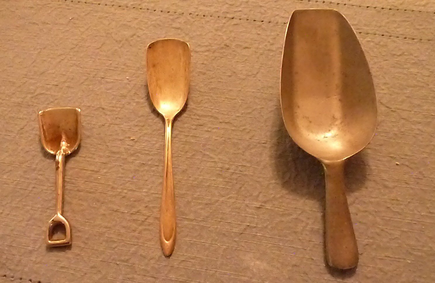 Three wooden kitchen utensils of different sizes on a beige surface.