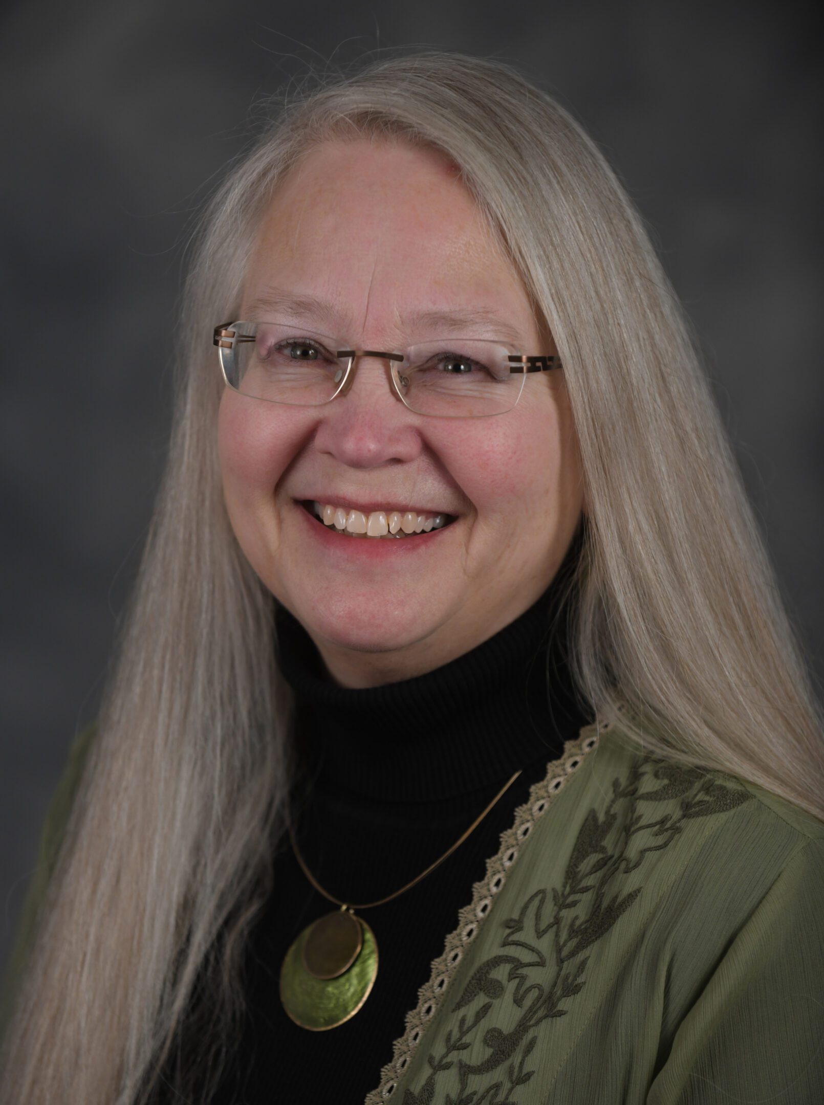 Smiling elderly woman with long gray hair and glasses.