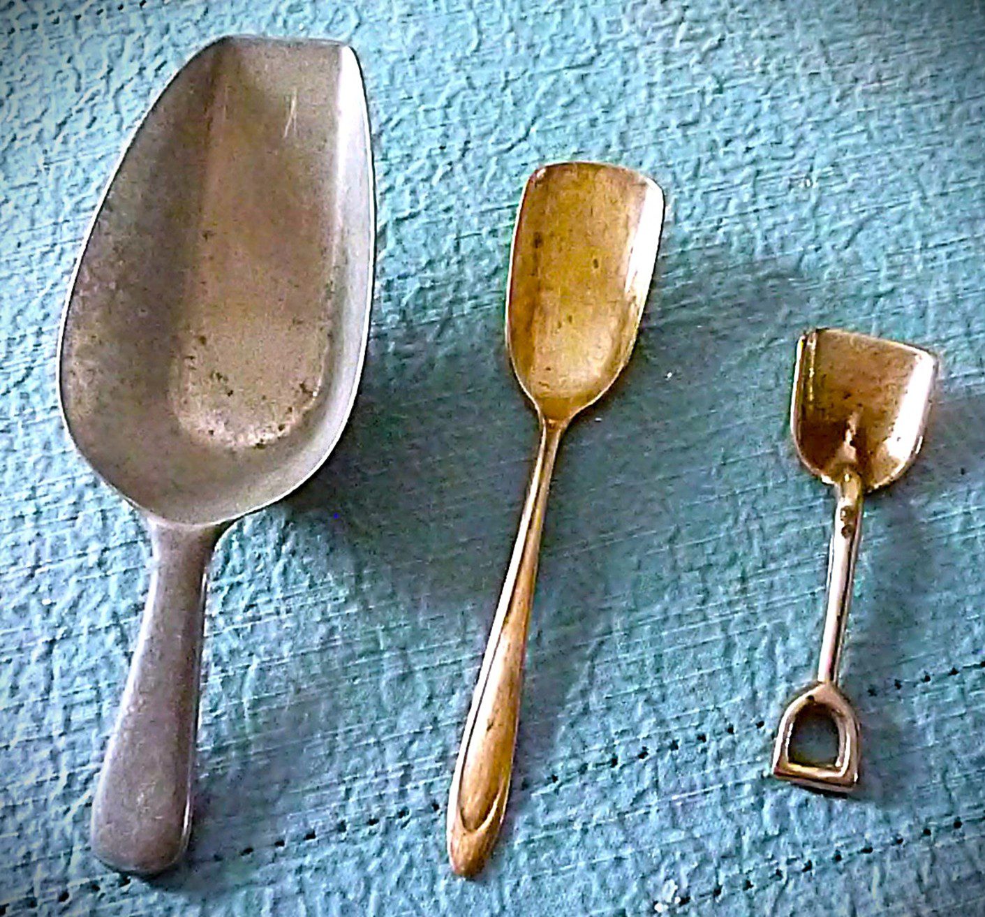 Three vintage scoops of different sizes on a textured blue cloth.